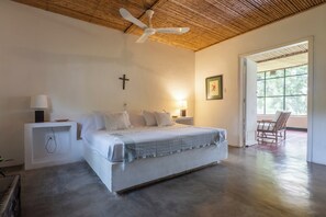 Ein Schlafzimmer mit einem Bett, Nachttischlampen, einem Kruzifix an der Wand und einer Tür zu einem Außenbereich.