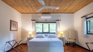 Una camera d'albergo con un letto, due lampade ai comodini, una sedia, una ventola a soffitto e una finestra con tende.