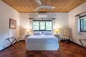 Ein Hotelzimmer mit einem Bett, zwei Nachttischlampen, einem Sessel, einem Deckenventilator und einem Fenster mit Vorhängen.