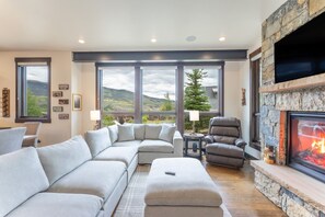 Ein modernes Wohnzimmer mit Kamin aus Stein, großen Fenstern und einem Ecksofa.