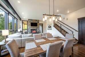 A modern living room with a fireplace, a dining area with a wooden table, and a staircase. - Pet Friendly Mountain Retreat | Private Hot Tub | Private Firepit | Direct Trail Access (Silverthorne)