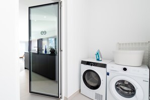 Ett modernt tvättrum med en tvättmaskin och en torktumlare med frontmatning, en glasdörr som leder till ett köksområde och en vit, kaklad vägg.
