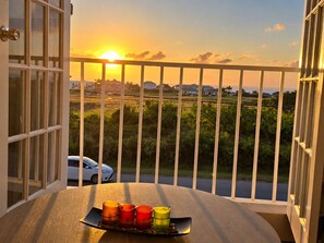 Een balkon met uitzicht op een zonsondergang, een auto op de straat en een dienblad met kaarsen.