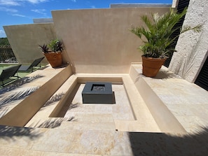 A sunlit outdoor area with a seating arrangement, a fire pit, and potted plants. - Super High Ceilings 2 BR, 2.5 Bath Apt. with plunge pool and terrace. (Tulum)