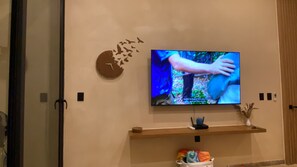 A television mounted on a wall with a clock and decorative wall art. - Super High Ceilings 2 BR, 2.5 Bath Apt. with plunge pool and terrace. (Tulum)