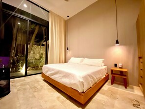 A modern bedroom with a large bed, a bedside table, and a view through a sliding glass door. - Super High Ceilings 2 BR, 2.5 Bath Apt. with plunge pool and terrace. (Tulum)
