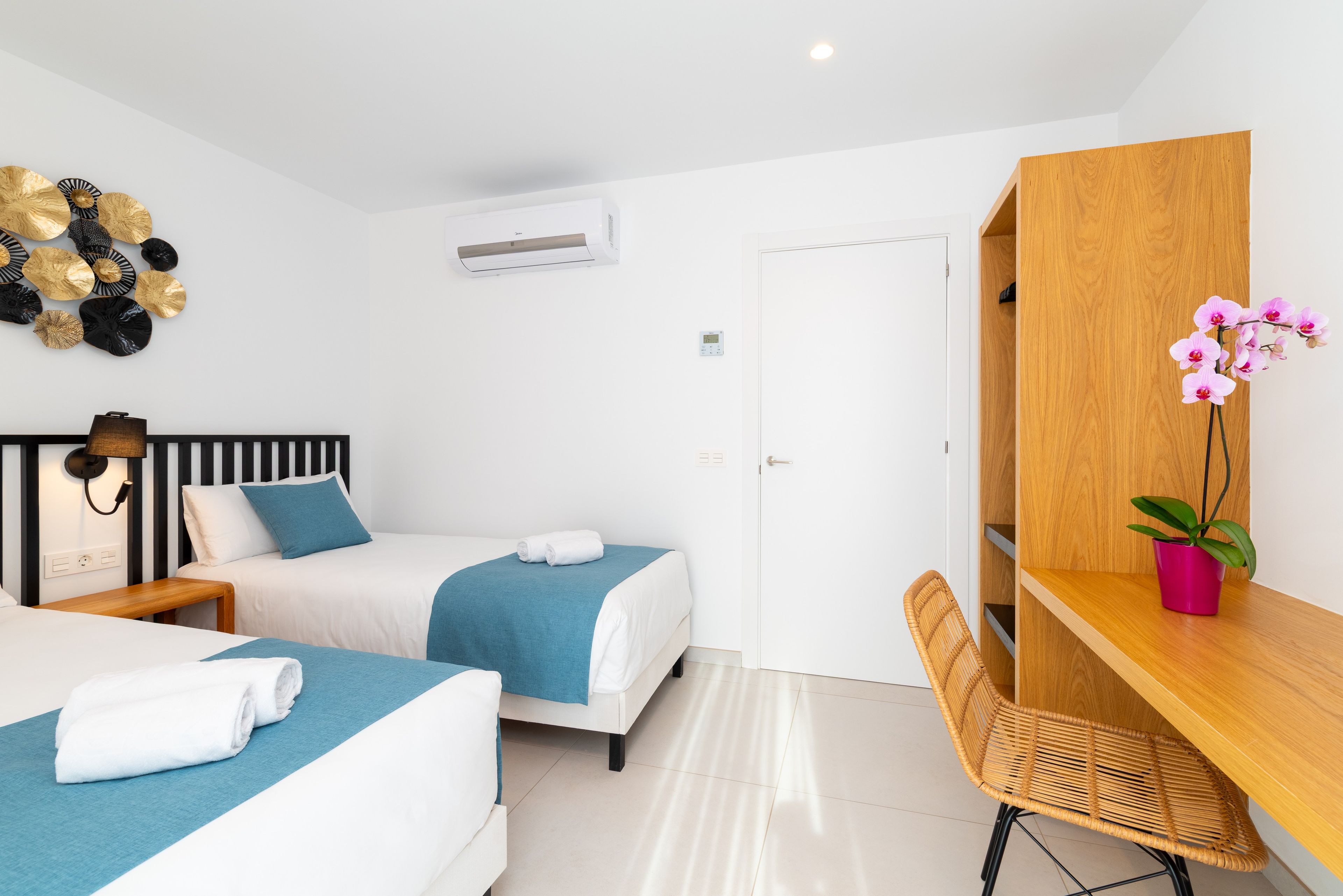 A modern hotel room with two beds, a desk, a chair, a wardrobe, and decorative wall art.