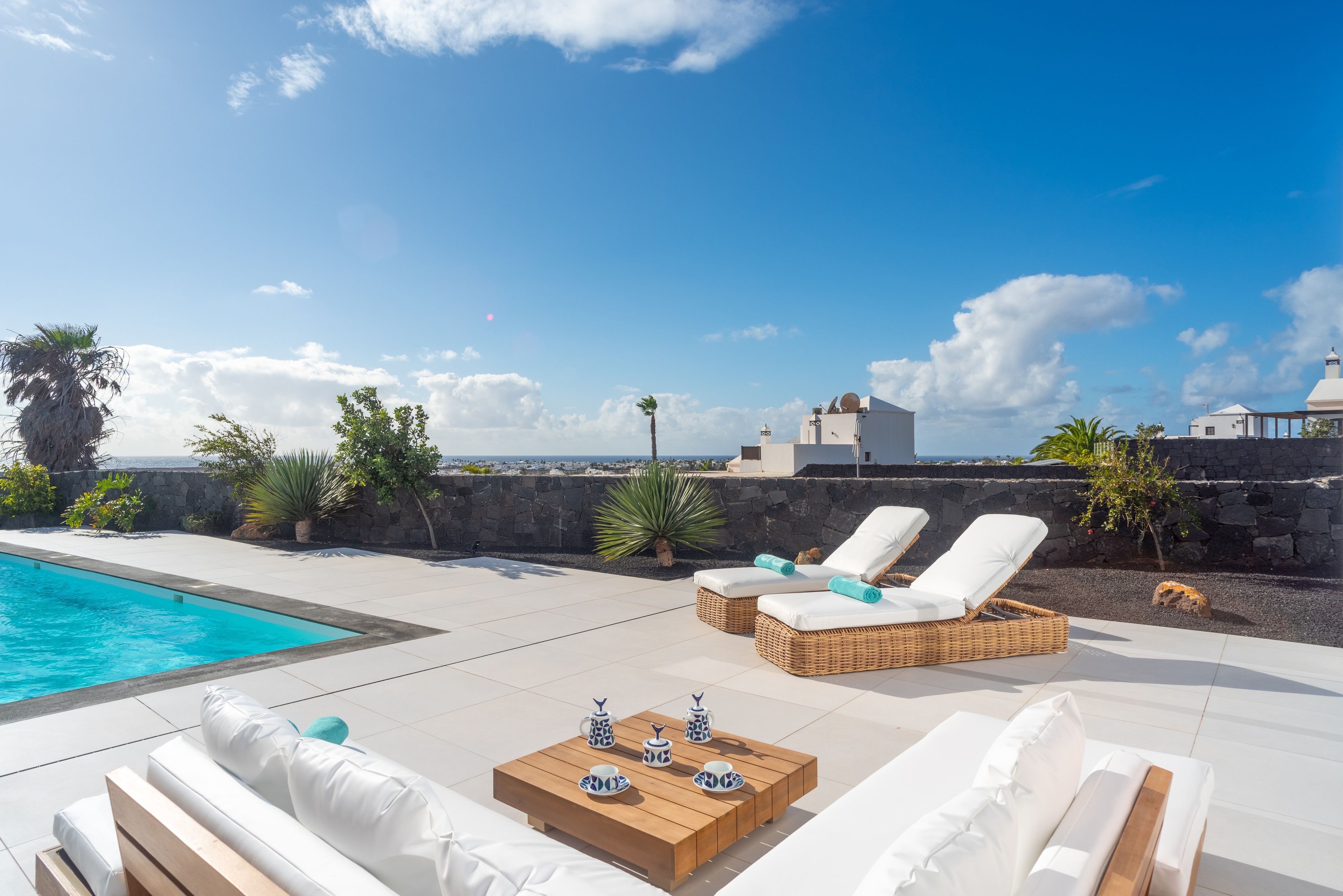 Zona de piscina con sillones, una mesa de madera con juego de té y vista al mar.