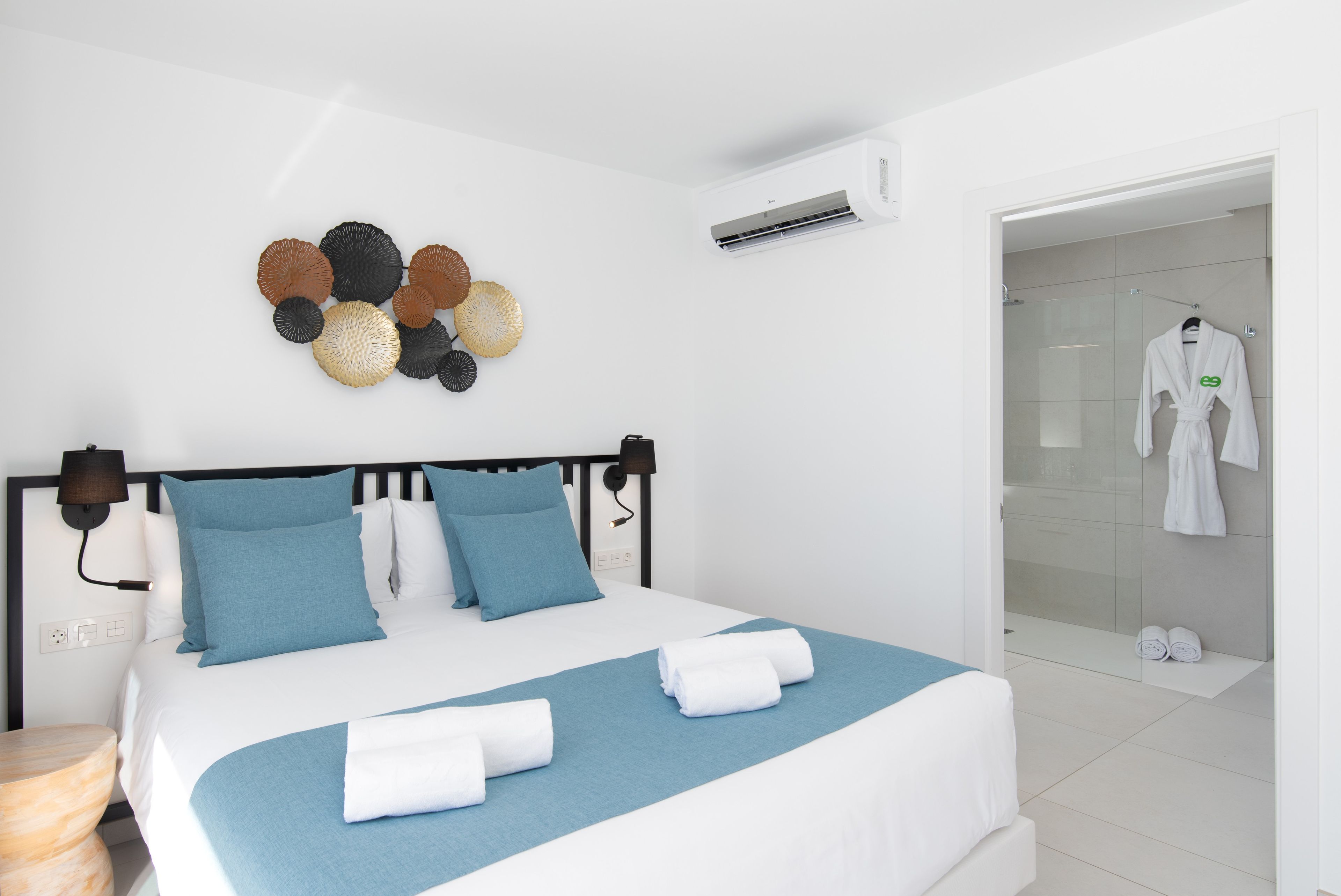 Habitación de hotel moderna con una cama, aire acondicionado montado en la pared, un adorno mural y un baño visible a través de una puerta abierta.