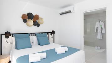 Habitación de hotel moderna con una cama, aire acondicionado montado en la pared, un adorno mural y un baño visible a través de una puerta abierta.