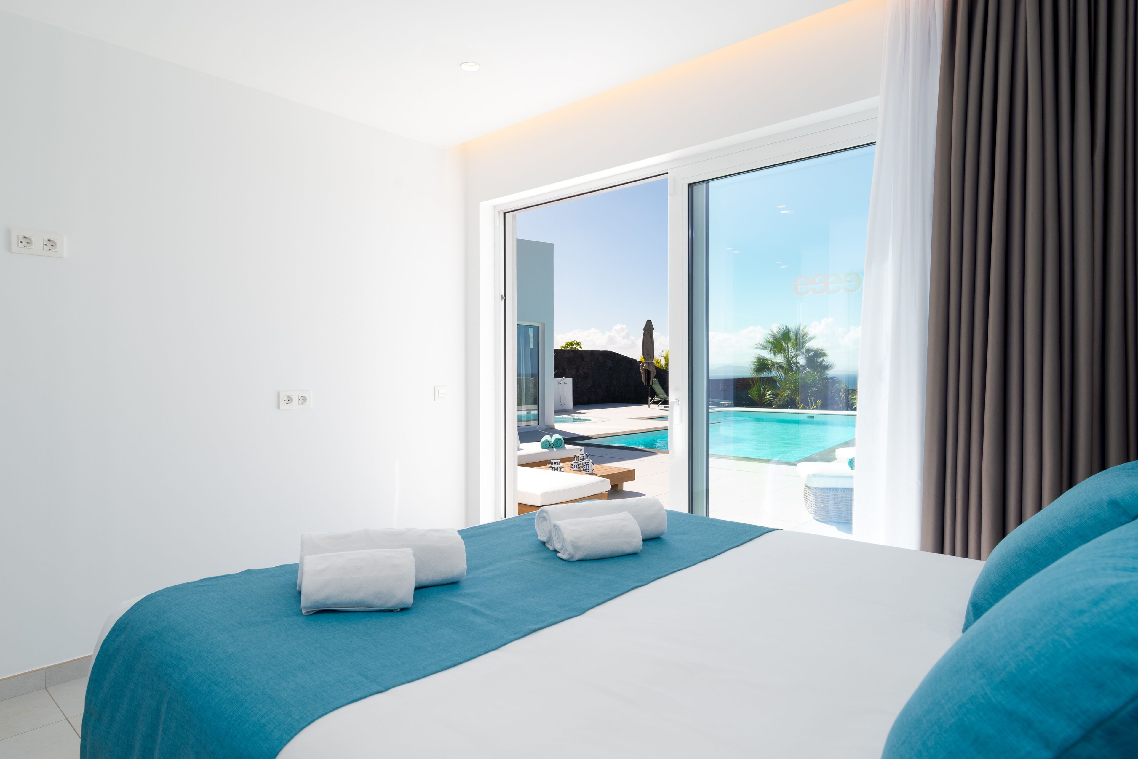 Ein modernes Hotelzimmer mit einem großen Bett, Blick auf einen Swimmingpool und einer Schiebetür zu einem Außenbereich.