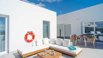 Un espacio exterior moderno con un sofá blanco, una mesa de centro de madera y un comedor.