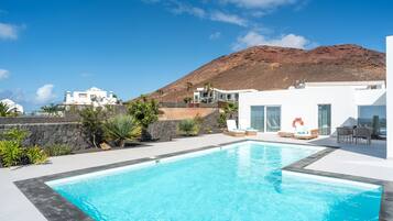 Una piscina con montañas al fondo, edificios blancos y cielo despejado.