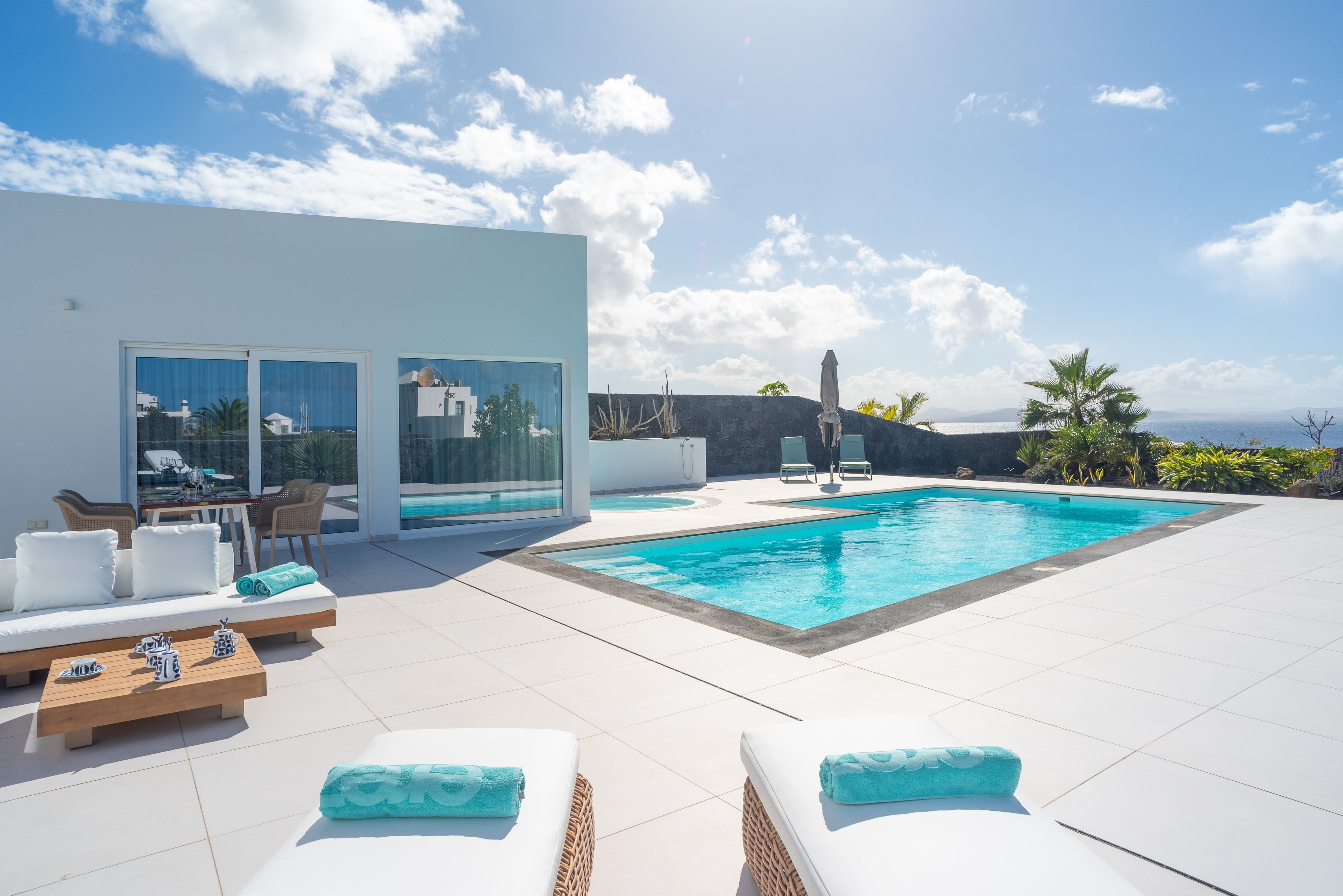 Un espace piscine extérieur moderne, doté de chaises longues et offrant une vue sur la mer.