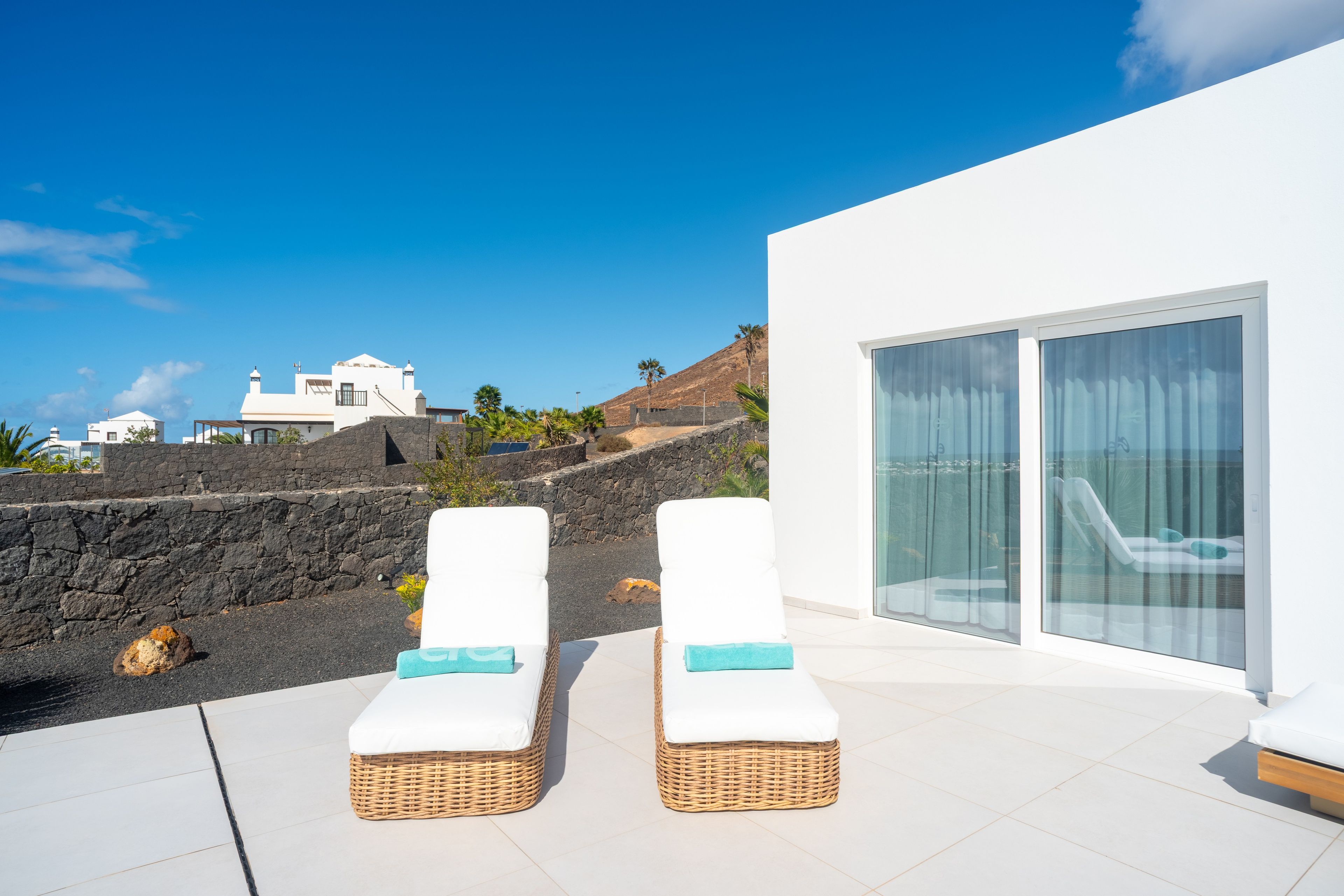 Un área de estar moderna al aire libre con dos sillones de mimbre, una pared de piedra y vistas del paisaje circundante.