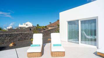 Un área de estar moderna al aire libre con dos sillones de mimbre, una pared de piedra y vistas del paisaje circundante.
