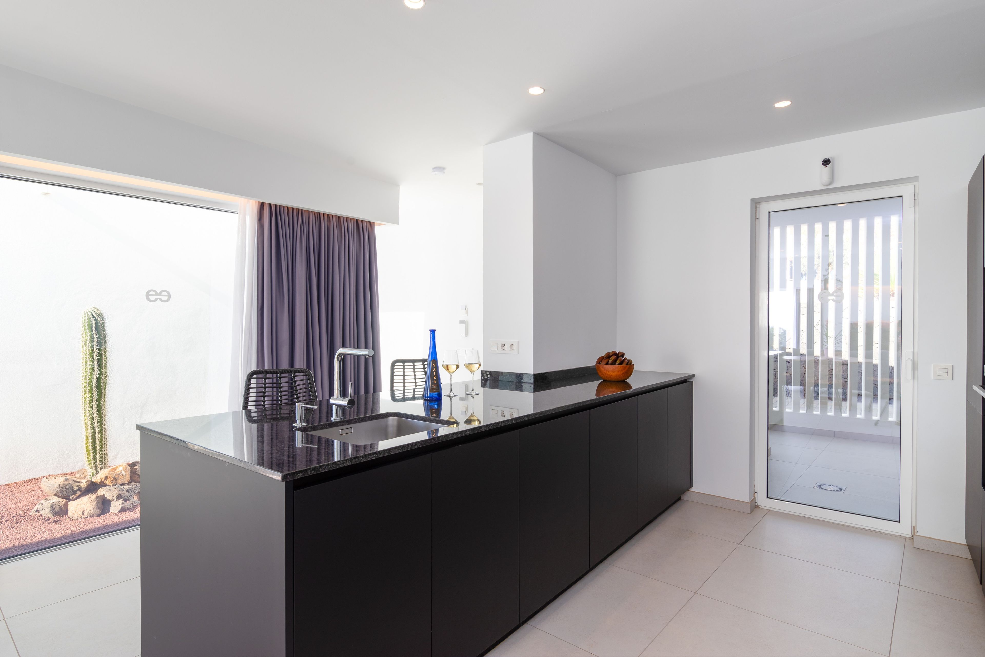 A modern kitchen with a black countertop, a built-in sink, and a glass door leading to a balcony.