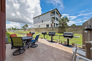An outdoor patio with a round table and chairs, barbecue grills, and a wooden fence. - Direct Oceanfront Condo, Top Floor, King, Heated Pools + Hot Tub, Sleeps 9, W... (Orange Beach)