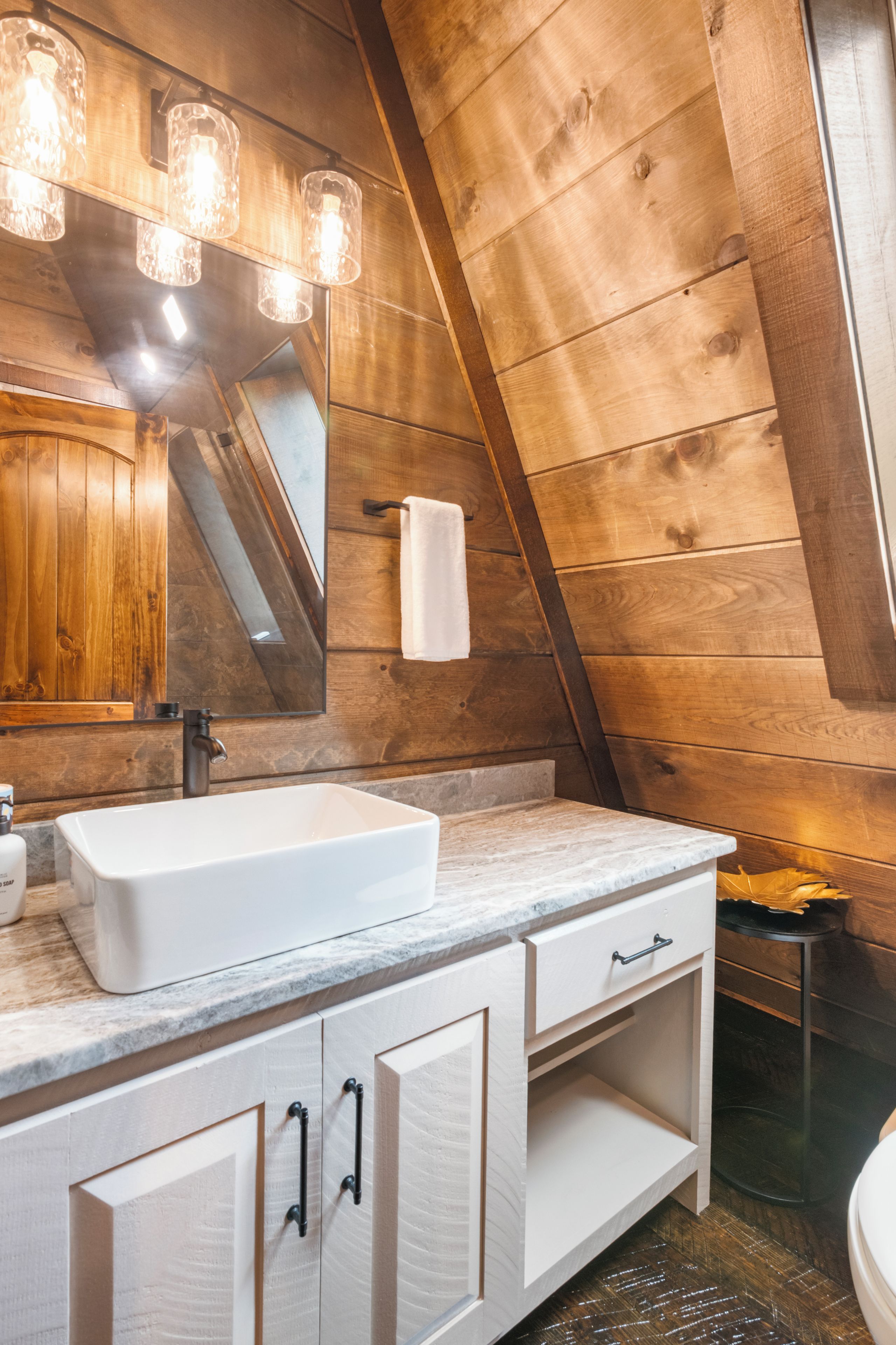 A bathroom with a white sink, wooden walls, and a mirror.