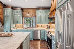 A modern kitchen with light blue cabinets, stainless steel appliances, and a large window.