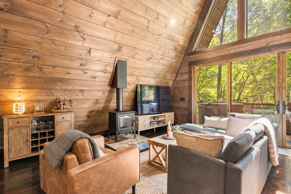 A cozy cabin interior with a wooden ceiling, a fireplace, a television, and a sofa.