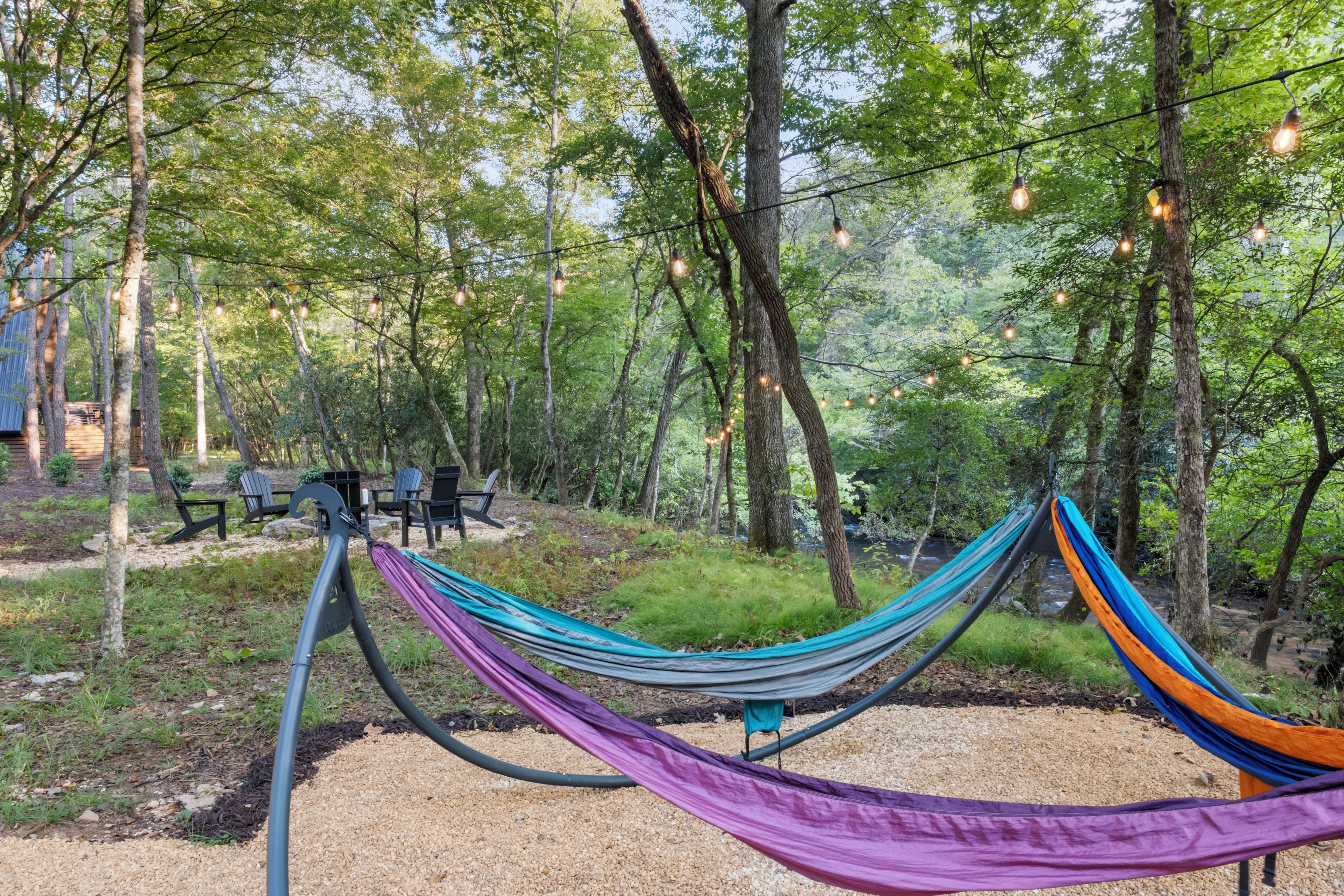 A hammock in a forested area with a gravel path and picnic tables.
