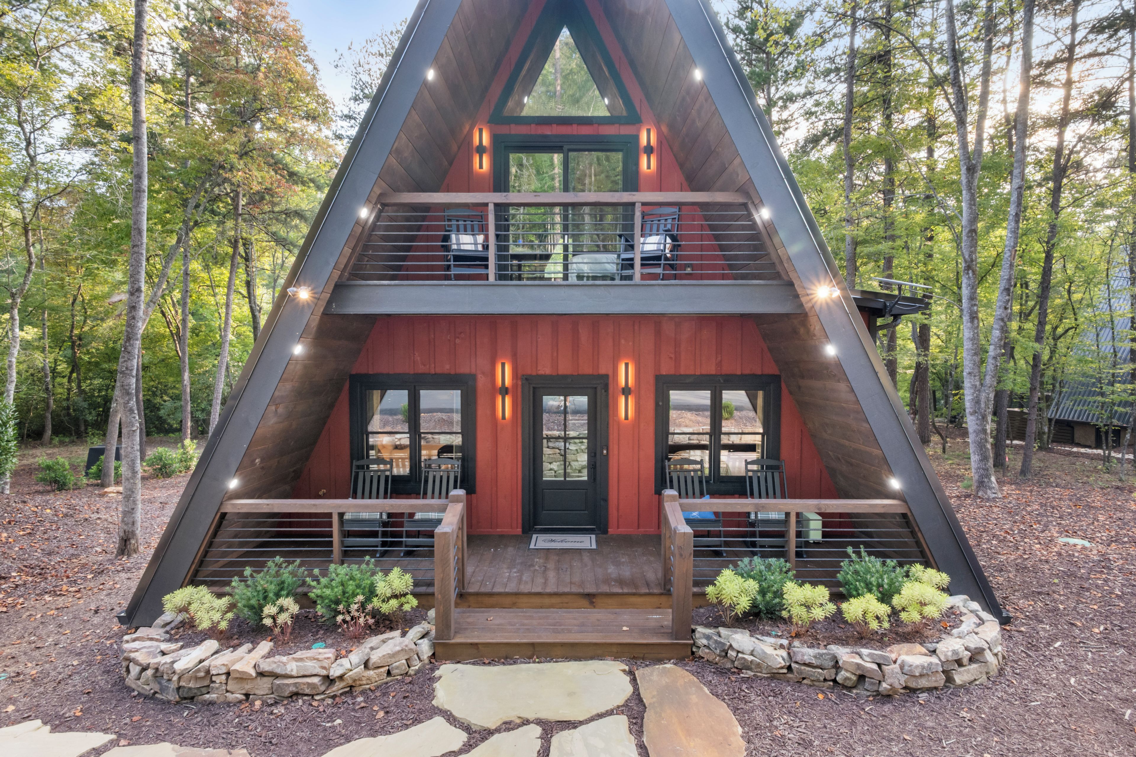 A modern, triangular-shaped cabin with a wooden exterior, two balconies, and a stone pathway leading to the entrance.