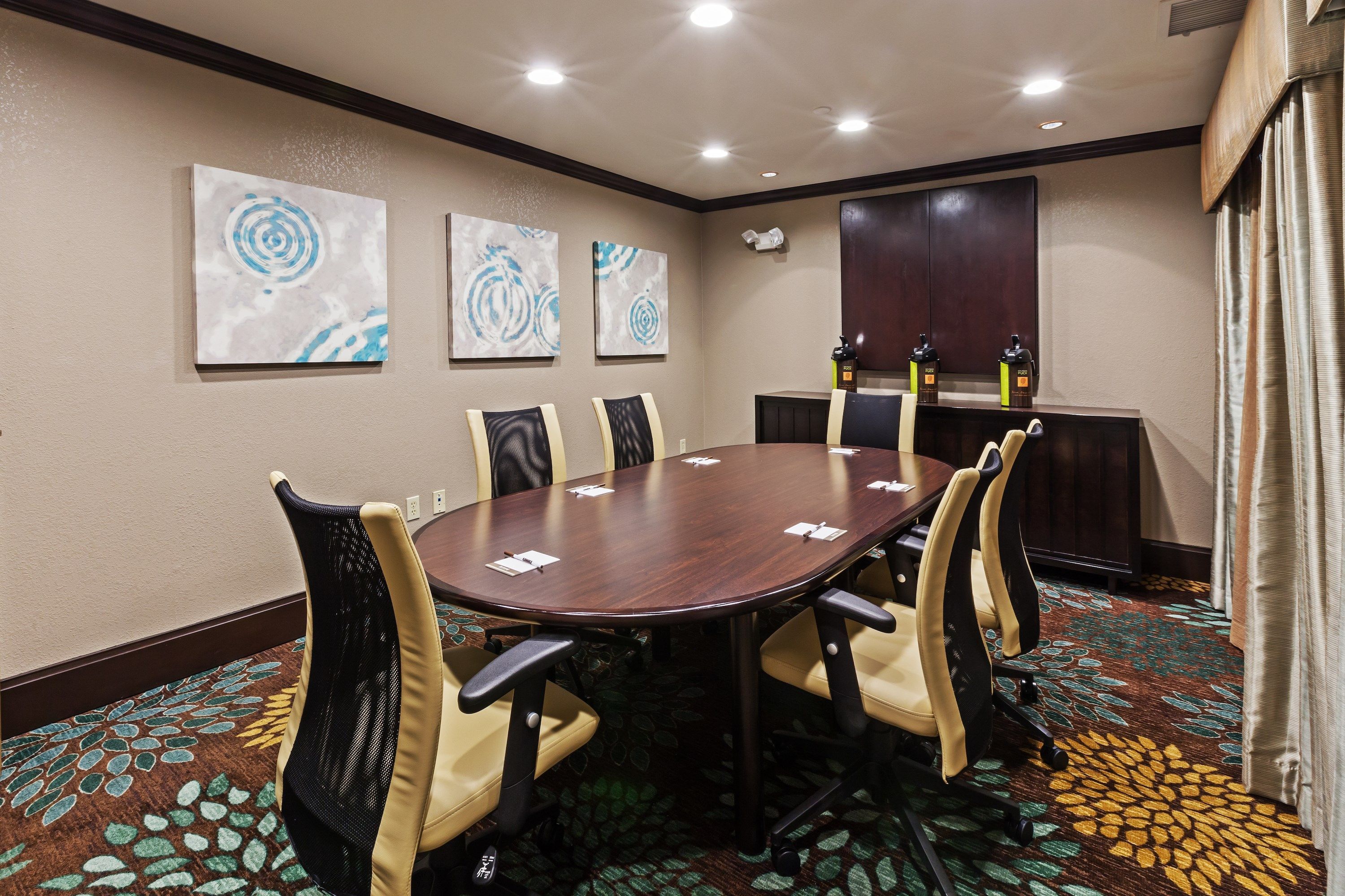 A conference room with a round table, six chairs, and three abstract wall art pieces.