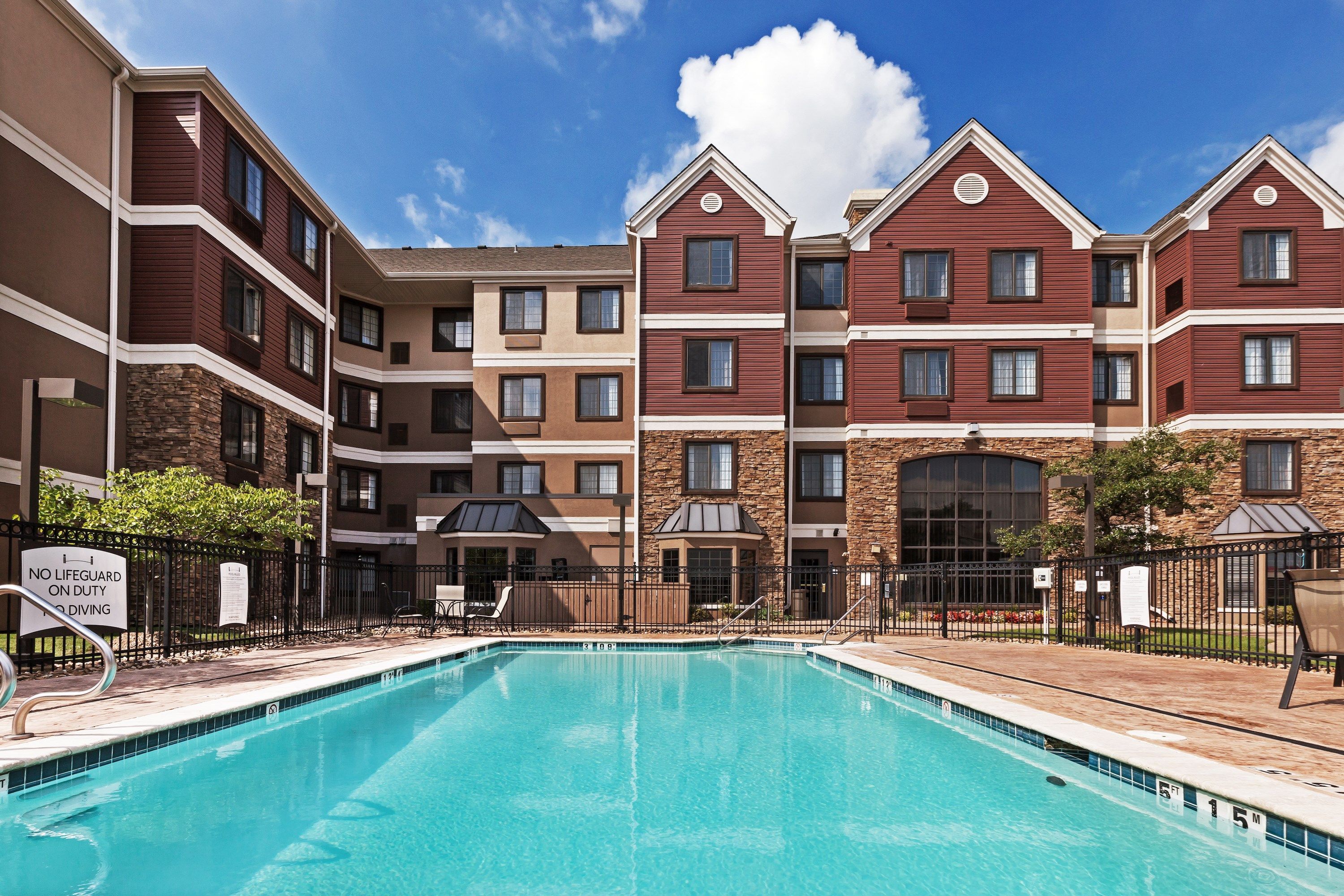 A pool area with a clear blue pool, surrounded by a brick building with multiple windows and balconies.