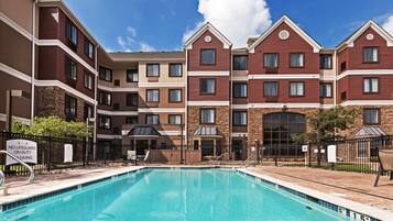 A pool area with a clear blue pool, surrounded by a brick building with multiple windows and balconies.