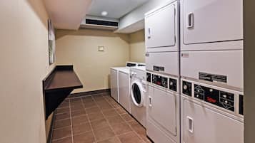 Une buanderie équipée de machines à laver et de sèche-linge superposés, d’une étagère fixée au mur et d’une bouche d’aération au plafond.