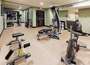 A gym with various exercise equipment, including treadmills, weight machines, and a bench.