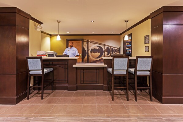 A hotel lobby with a reception desk, two bar stools, and a large wall mural.