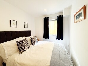 A bedroom with a bed, two framed pictures on the wall, a window with curtains, and a picture frame on the wall. - Two bedroom, two bathroom apartment with terrace close to Torquay seafront. (Torquay)