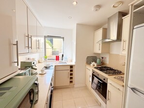 A compact kitchen with a gas stove, a coffee machine, and a window providing natural light. - Two bedroom, two bathroom apartment with terrace close to Torquay seafront. (Torquay)