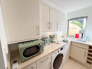 A compact kitchen with a washing machine, a microwave, and a toaster. - Two bedroom, two bathroom apartment with terrace close to Torquay seafront. (Torquay)