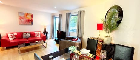 A modern living room with a red sofa, a dining table set for two, and a large window with curtains.