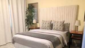 Un dormitorio ordenado con cama, mesitas de noche, una lámpara y una planta en maceta.