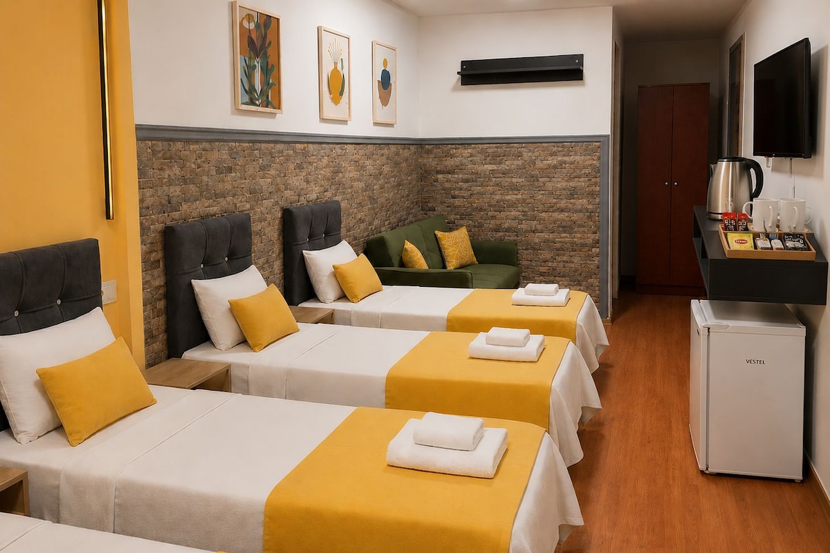 Habitación de hotel con tres camas, un sofá, una cafetera y un televisor.