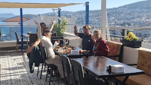 En terrass med ett bord dukat för fyra personer, utsikt över en stad och en klar himmel.