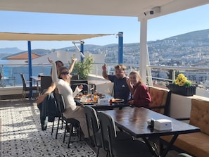 Una terraza con mesa lista para cuatro personas, vista a un paisaje urbano y cielo despejado.