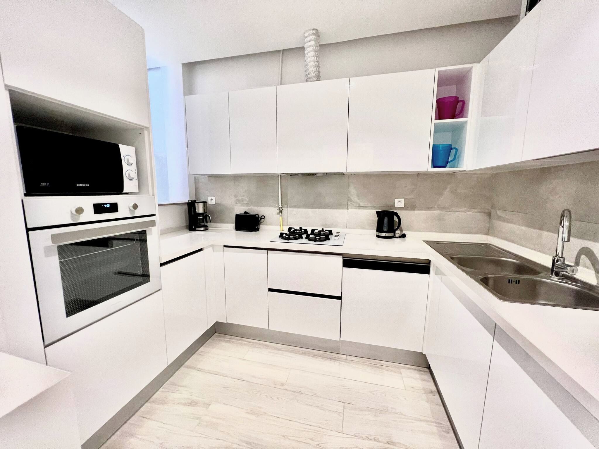 A modern kitchen with white cabinets, a built-in oven, a coffee maker, and a sink.