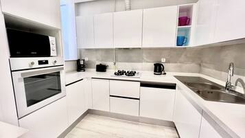 A modern kitchen with white cabinets, a built-in oven, a coffee maker, and a sink.