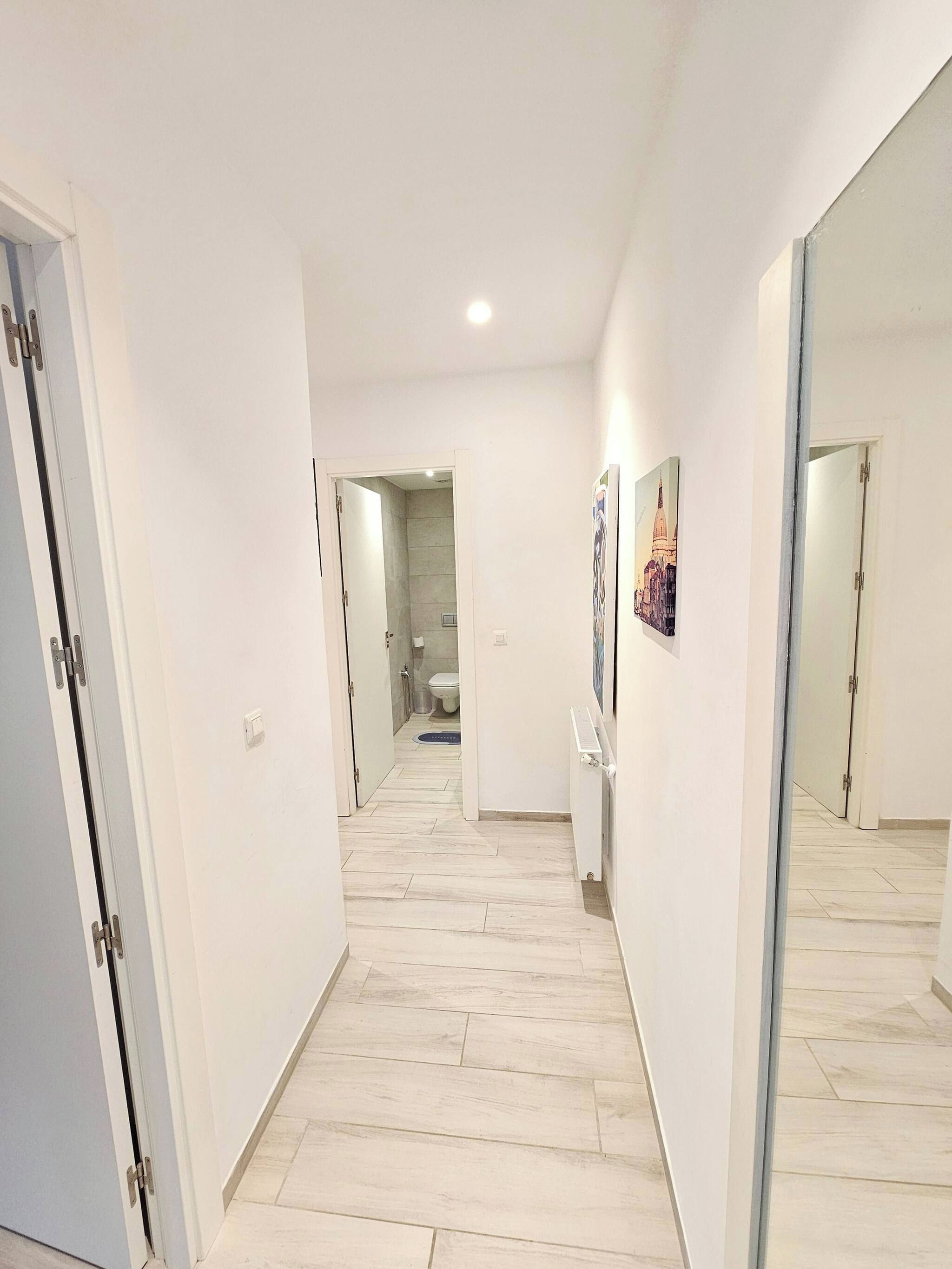 Um corredor com paredes brancas, chão de azulejos e portas que dão para outros quartos.