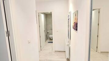 Um corredor com paredes brancas, chão de azulejos e portas que dão para outros quartos.
