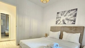 A neatly made bed with white linens and a rolled towel, a wooden floor, a wall-mounted abstract art piece, and a hanging light fixture. - Contemporary Haven in the Heart of La Marsa (La Marsa)