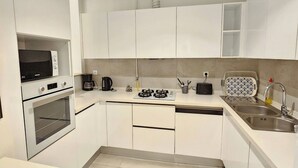 Cuina moderna amb armaris blancs, forn de mur, microones, fogó de gas i rentatge.