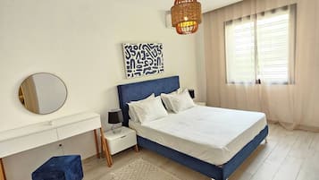 A bedroom with a bed, bedside tables, a mirror, a rug, and a window with curtains.