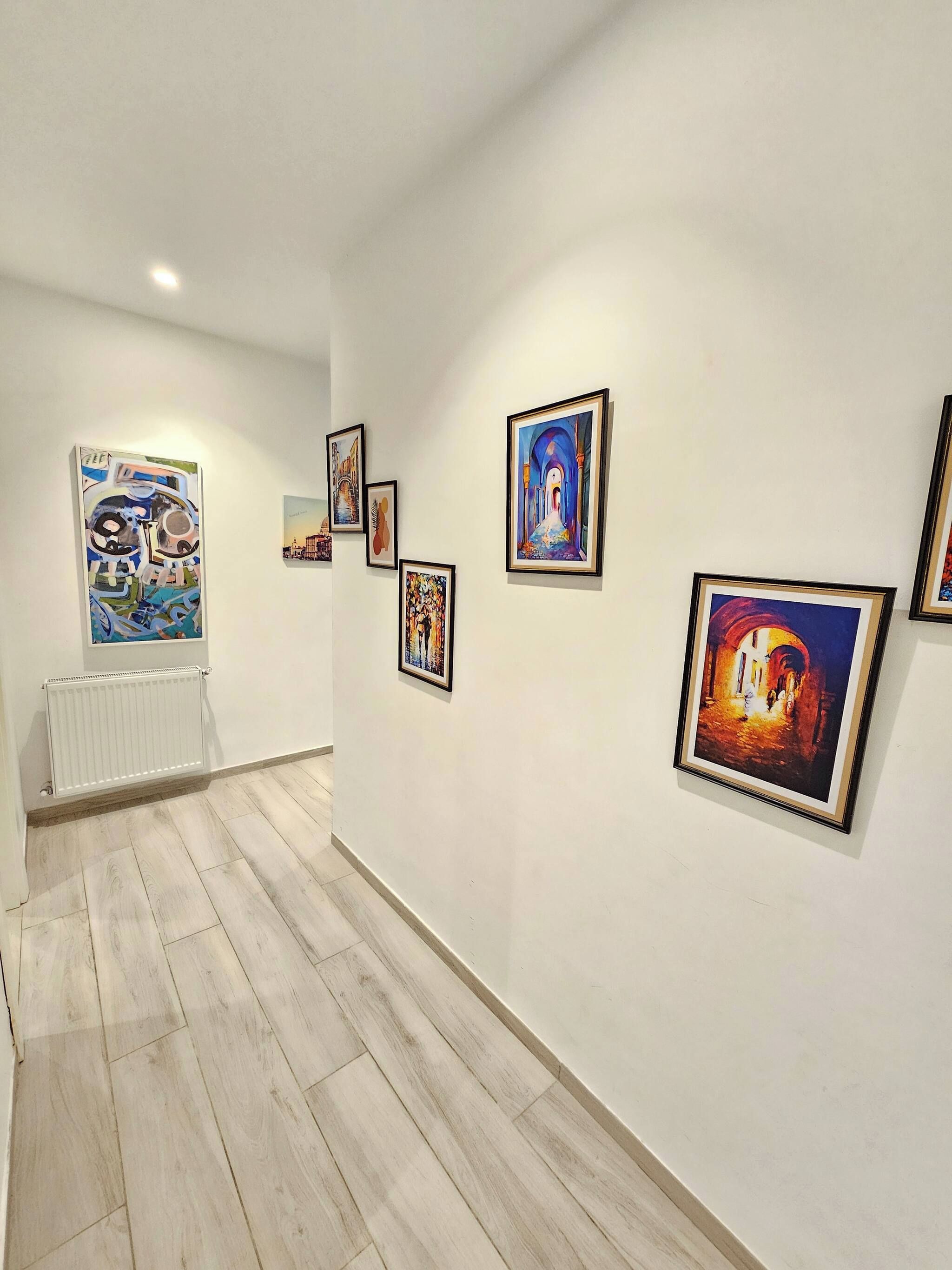 An art gallery with several framed paintings on the walls and a radiator on the left.