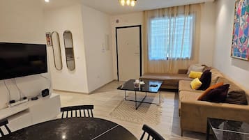 Una sala de estar moderna con una mesa de comedor redonda, un juego de sofás, un televisor y una lámpara de techo.